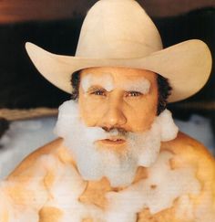 a man wearing a cowboy hat with foam on his face and chest, sitting in the snow