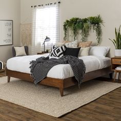 a bed with white sheets and pillows on top of it in a room filled with plants