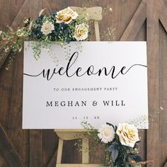 a welcome sign with flowers and greenery sits on top of a wooden easer