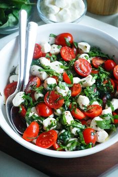 a salad with tomatoes, mozzarella and spinach is in a white bowl