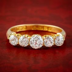 a five stone diamond ring sitting on top of a red surface with gold trimming