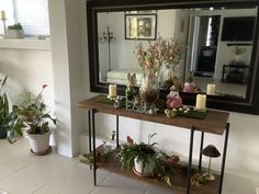 a table with plants and candles on it in front of a mirror that is reflecting the room