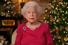 an older woman sitting in front of a christmas tree wearing a red sweater and pearls