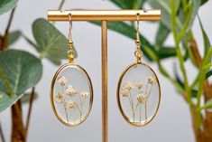 The delicate white baby's breath bundles are hand pressed, delicately arranged, and preserved in resin inside the gold, oval bezel. This elegant pair is lightweight, and can be worn all day without discomfort! They are made with hypoallergenic gold metal ear wire and crystal clear resin, allowing every detail of the baby's breath to be seen. While all pairs are assembled similarly, each flower is unique, making every pair one of a kind! Due to the products handmade nature, please understand that Delicate White Jewelry With Natural Inclusions, Delicate White Diamond Jewelry With Natural Inclusions, White Oval Earrings As Gift, Oval White Jewelry With Natural Inclusions, White Oval Jewelry With Natural Inclusions, Anniversary Jewelry With Pressed Flowers, Anniversary Jewelry With Pressed Flowers In White, White Earrings With Pressed Flowers, Dainty White Earrings With Pressed Flowers