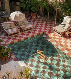 a person swimming in a pool with chairs and umbrellas