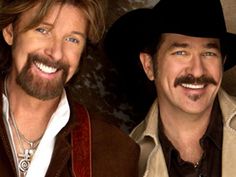 two men in cowboy hats are smiling at the camera and one is wearing a vest