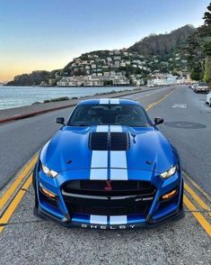 a blue and white sports car parked on the side of the road next to water