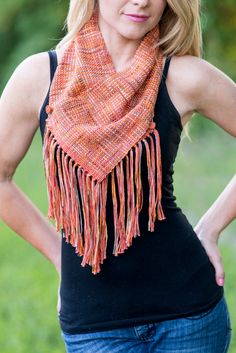 a woman wearing a scarf with fringes on her neck and black tank top standing in front of green grass