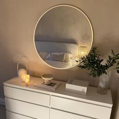 a white dresser with a round mirror above it and a plant on top of it