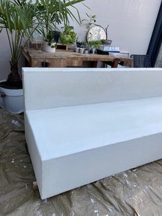 a white bench sitting on top of a bed next to a potted palm tree