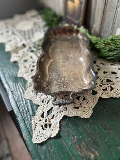 a metal tray sitting on top of a wooden table next to a pine branch and lace doily