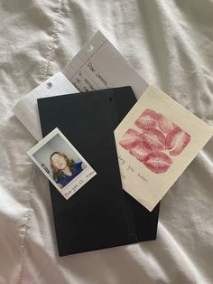 two envelopes, one with a stamp and the other with lipstick on them are laying on a bed