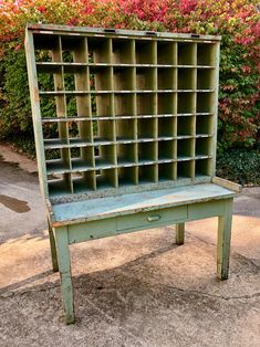 an old green bookcase sitting on top of a cement ground next to bushes and flowers