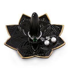 a black and gold ring holder with two pearls on the bottom, and a green jewel in the middle