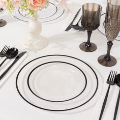 the table is set with black and white plates, silverware, and pink flowers