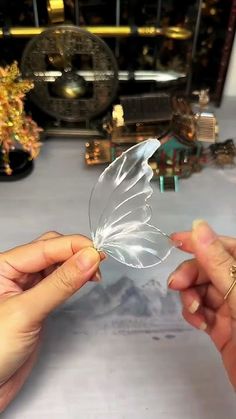 two hands holding a clear butterfly on top of a table