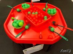 a red tray with green candies and spoons in it on top of a table