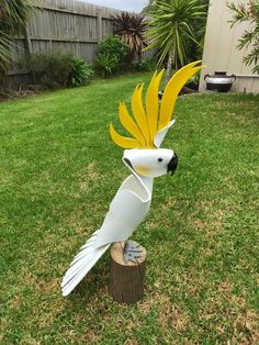 a white bird with yellow feathers sitting on top of a wooden stump in the grass