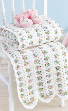 a crocheted blanket with two teddy bears sitting on top of it next to a white rocking chair