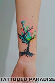 a tree tattoo on the arm with watercolor paint splatters all over it