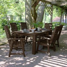 an outdoor dining table and chairs set up under a pergolated area with trees in the background