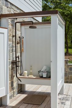 an outdoor shower on a wooden deck next to a brick wall and tree in the background