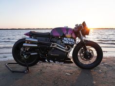 a motorcycle parked on top of a beach next to the ocean at sunset or sunrise