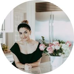 a woman in a black dress sitting at a kitchen counter with pink flowers on the counter