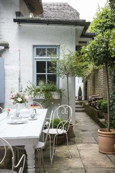 a white table and chairs sitting in front of a building with potted plants on it