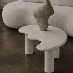 a white table with a vase sitting on it's top next to a couch