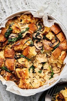 a casserole dish with mushrooms and spinach in it on a marble surface