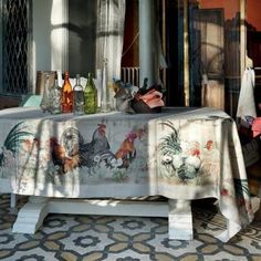 a table covered with roosters and flowers on top of a patterned rug in front of a window