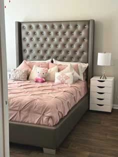 a bed with pink sheets and pillows in a bedroom next to a night stand that has a lamp on it