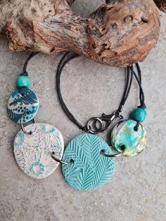 three different necklaces with turquoise and white designs on black cord hanging from a piece of driftwood