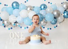 a baby sitting in front of a cake and balloons