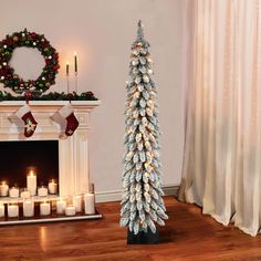 a white christmas tree in front of a fireplace with lit candles on the mantel