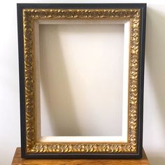 an ornate gold and black frame sitting on top of a wooden shelf next to a white wall