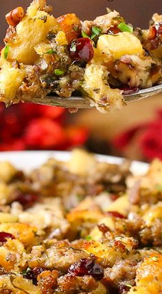 a spoon full of stuffing being lifted from a casserole dish with cranberries