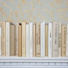 a row of books sitting on top of a white book shelf next to a wall