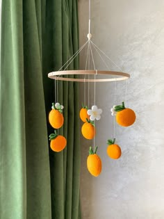 an orange mobile hanging from a curtain with flowers and fruit attached to the strings above it