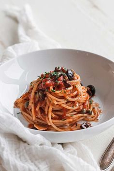 a white bowl filled with pasta and olives on top of a table next to a fork