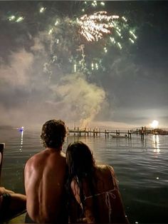 two people sitting on a dock watching fireworks