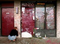 a person kneeling down in front of a building with graffiti on the walls and doors