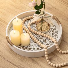 three candles are on a tray with rosary beads and a flower in a glass vase