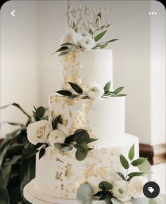 a wedding cake with white flowers and greenery on the top tier is decorated with gold leaf