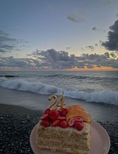 a piece of cake with strawberries on it sitting on a plate near the ocean