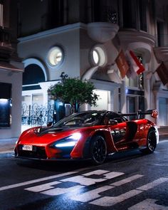 a red sports car parked in front of a building at night with its lights on