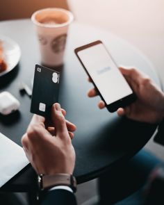 two people are sitting at a table with their cell phones and one is holding a credit card