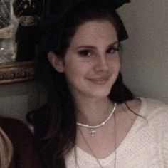 a young woman wearing a white sweater and black bow in her hair smiling at the camera