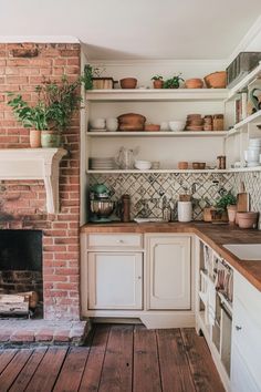 a brick fireplace in a kitchen next to white cupboards and shelves with plants on them